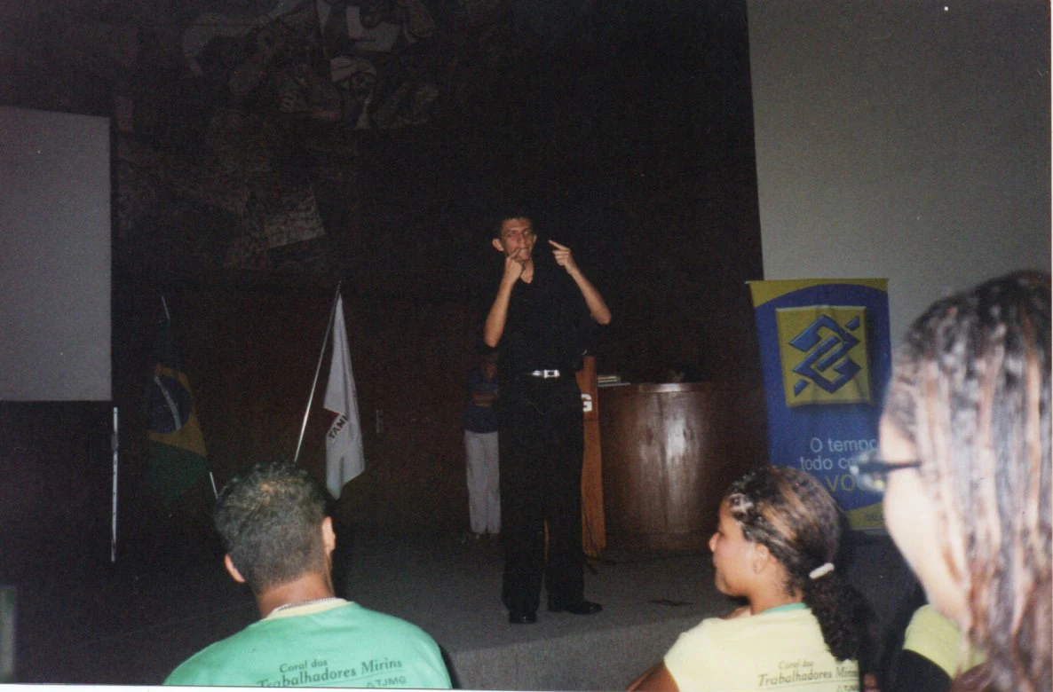Madson Barreto jovem interpretando em Libras no palco, num evento de formação de jovens aprendizes surdos, 2008